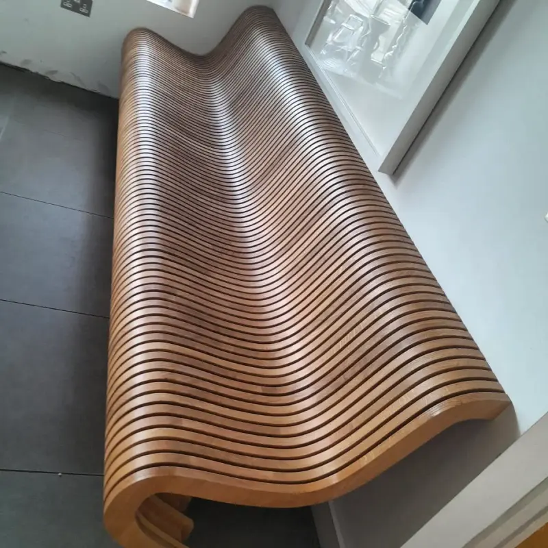 Slatted timber bench seen from one end, showing its wave profile