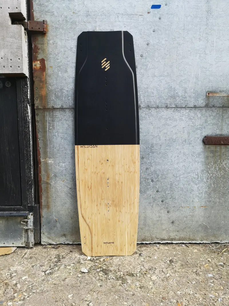 Kiteboard with a black and natural timber top, standing against a wall